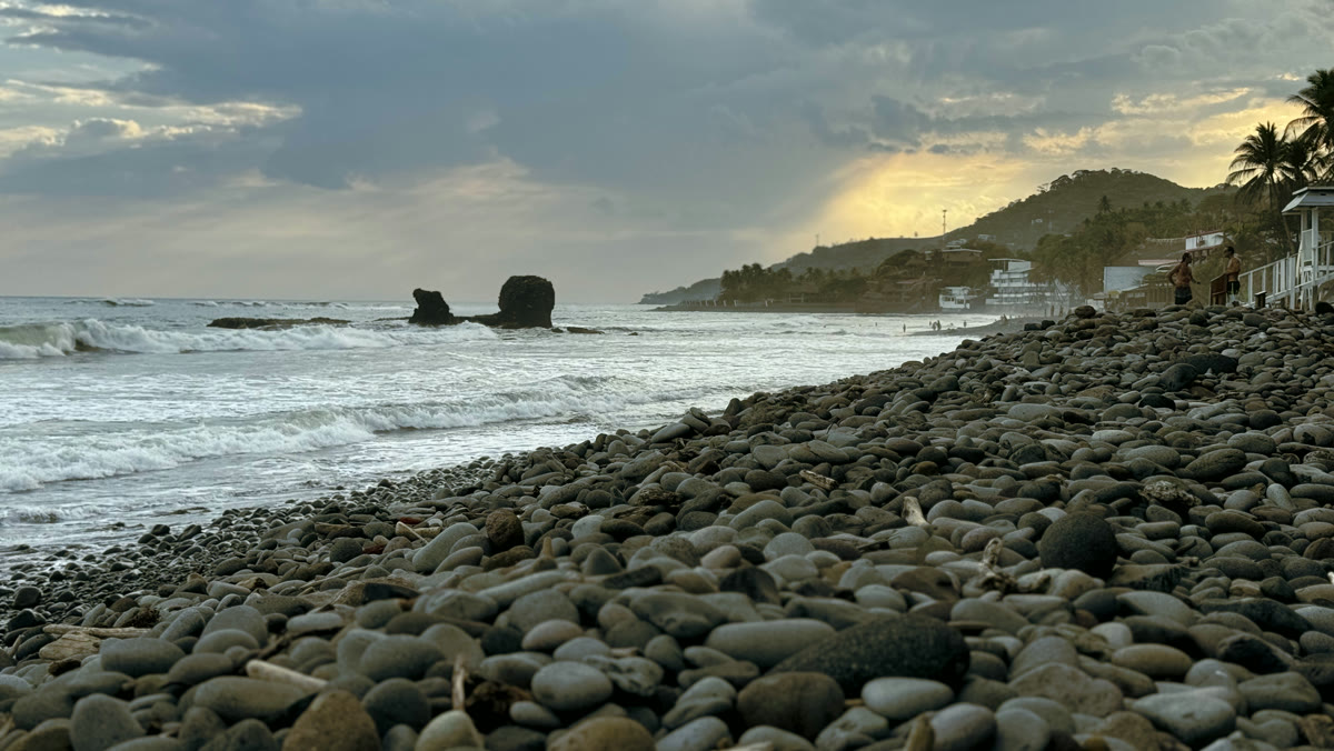 El Tunco al atardecer: playa de piedras, olas y el pueblo sobre la colina, en La Libertad.